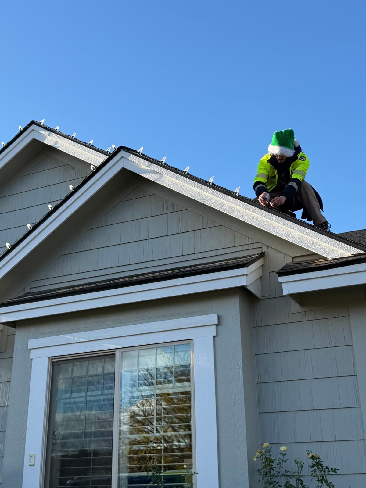 Installer in a green elf hat connecting C9 roofline lights on a clear day