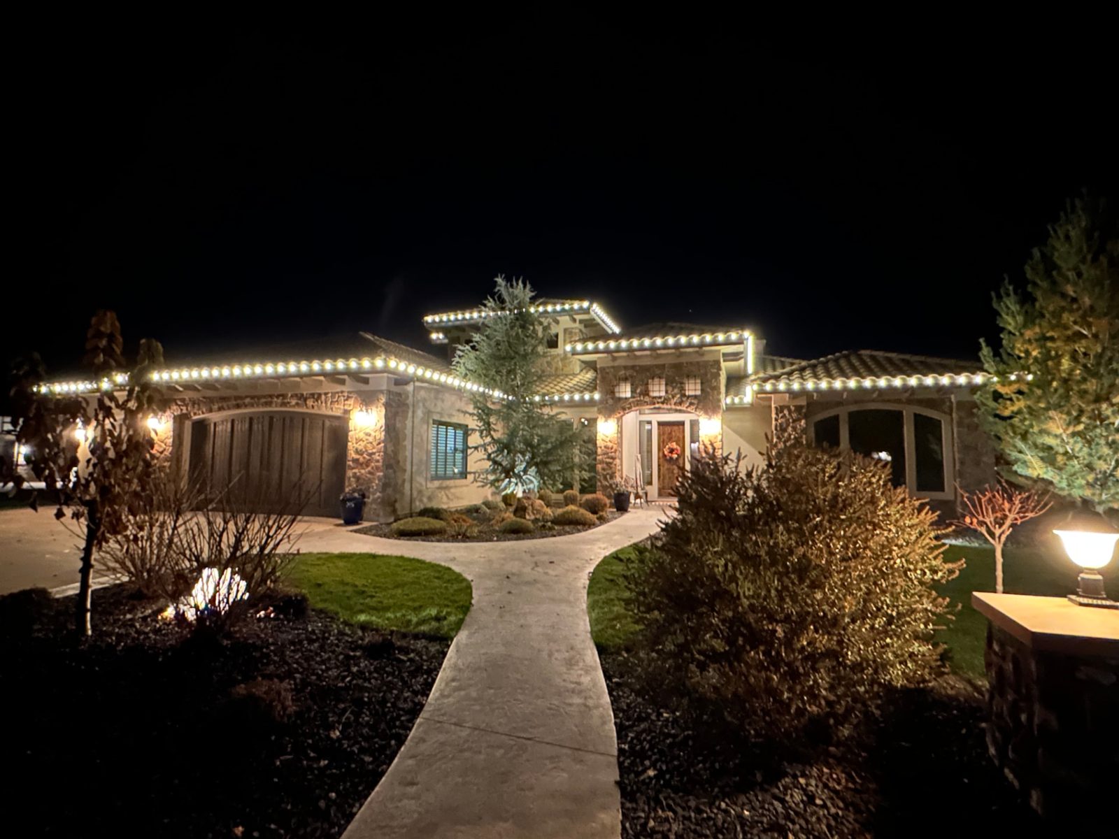 Warm white C9 Christmas lights on a tile-roof stone home in Idaho