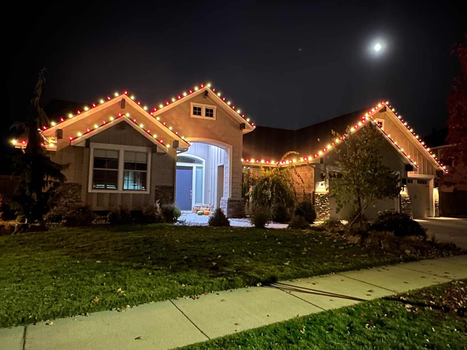 Red and warm white Christmas lights on gabled rooflines under a full moon