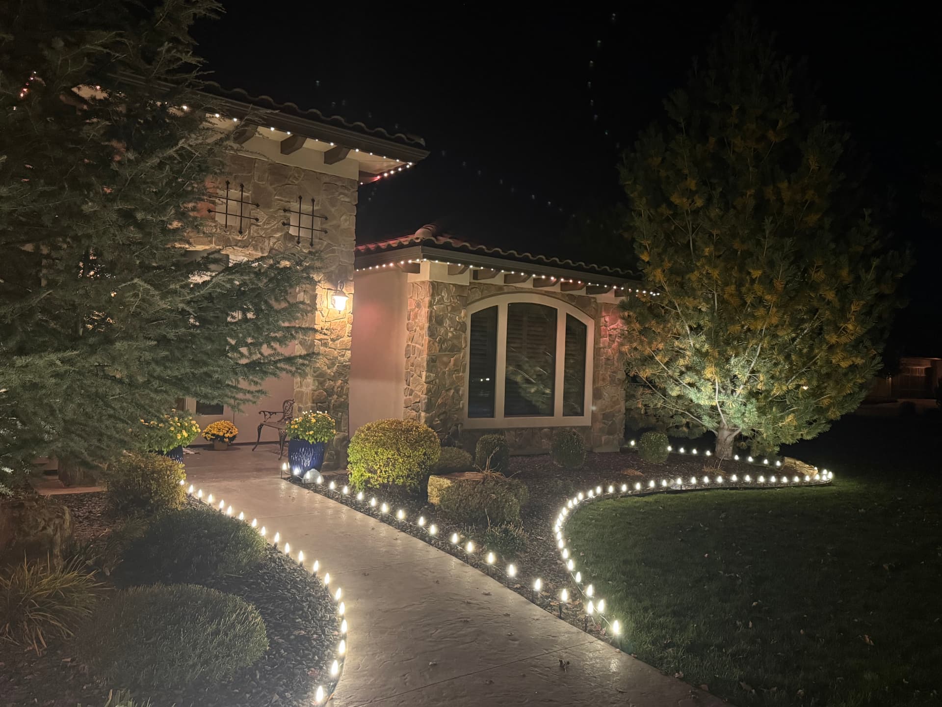 Warm white C9 walkway lights and tile roofline lighting on a stone home