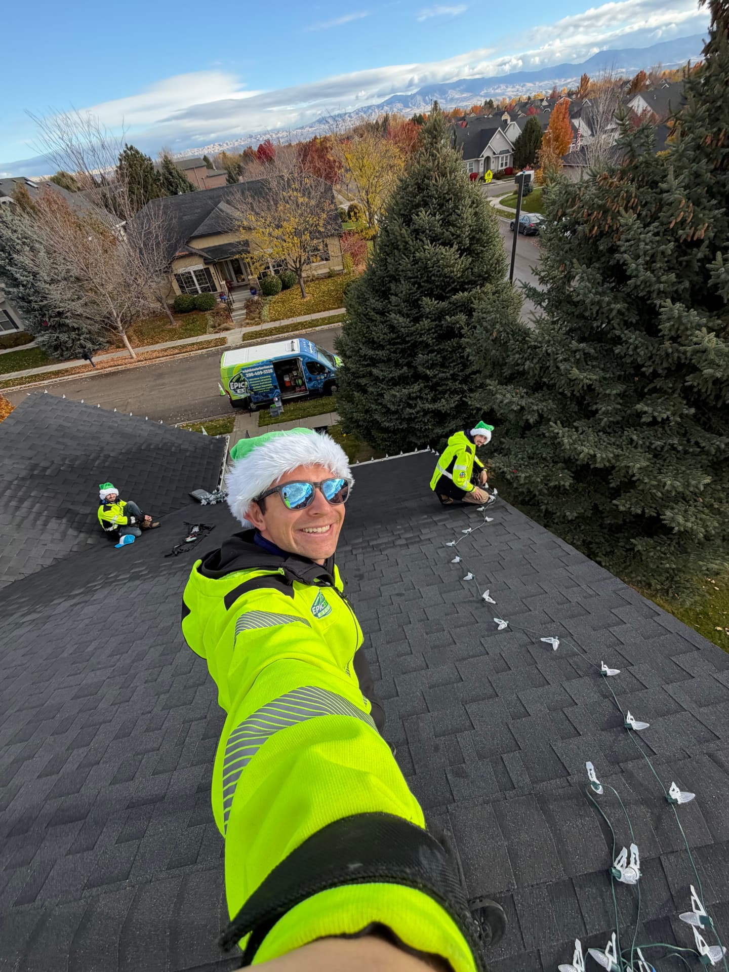 Epic Exterior Lighting crew in elf hats on a roof with the Boise foothills behind