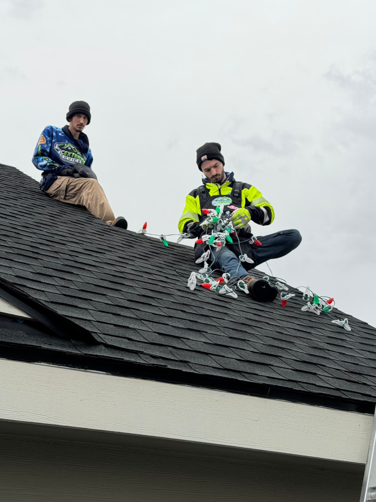 Two crew members on a roof sorting red and green C9 Christmas light strands