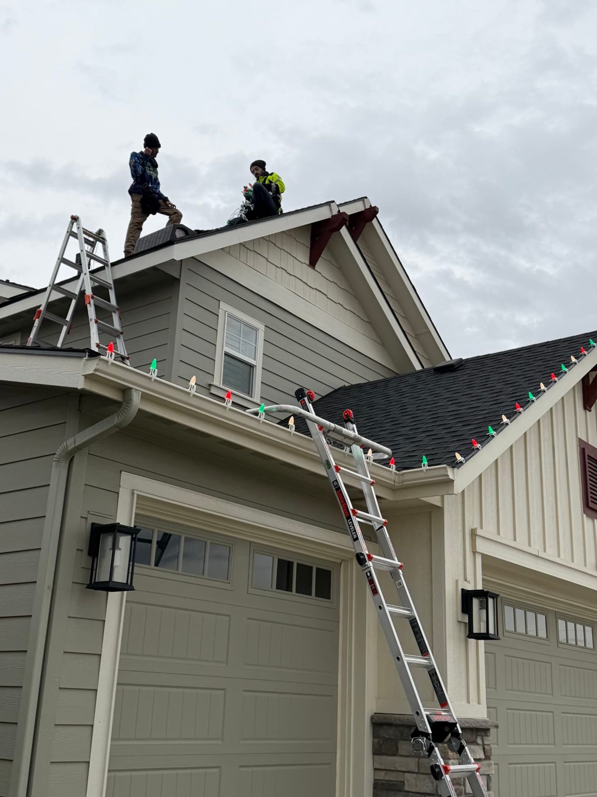 Two Epic Exterior Lighting installers on a two-story roof clipping red, green and white C9 lights to the gutters