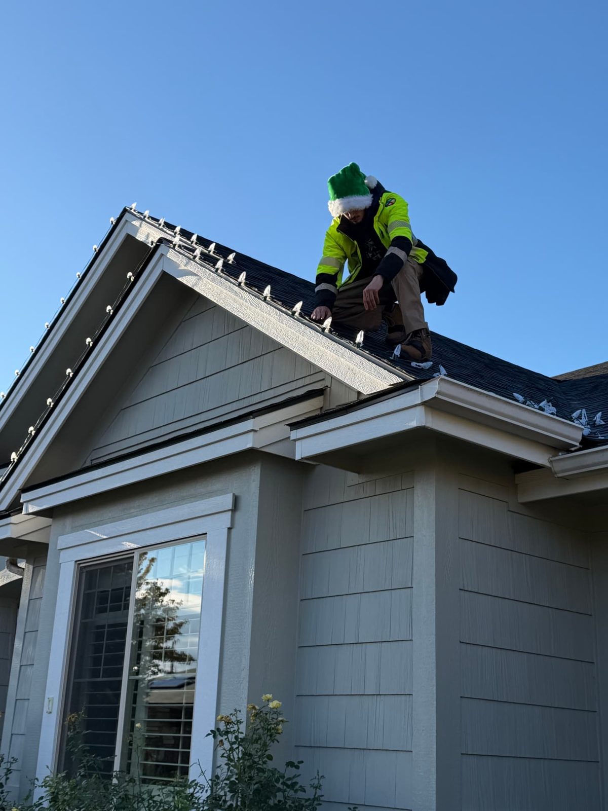 Installer in an elf hat clipping white C9 bulbs along a gable edge