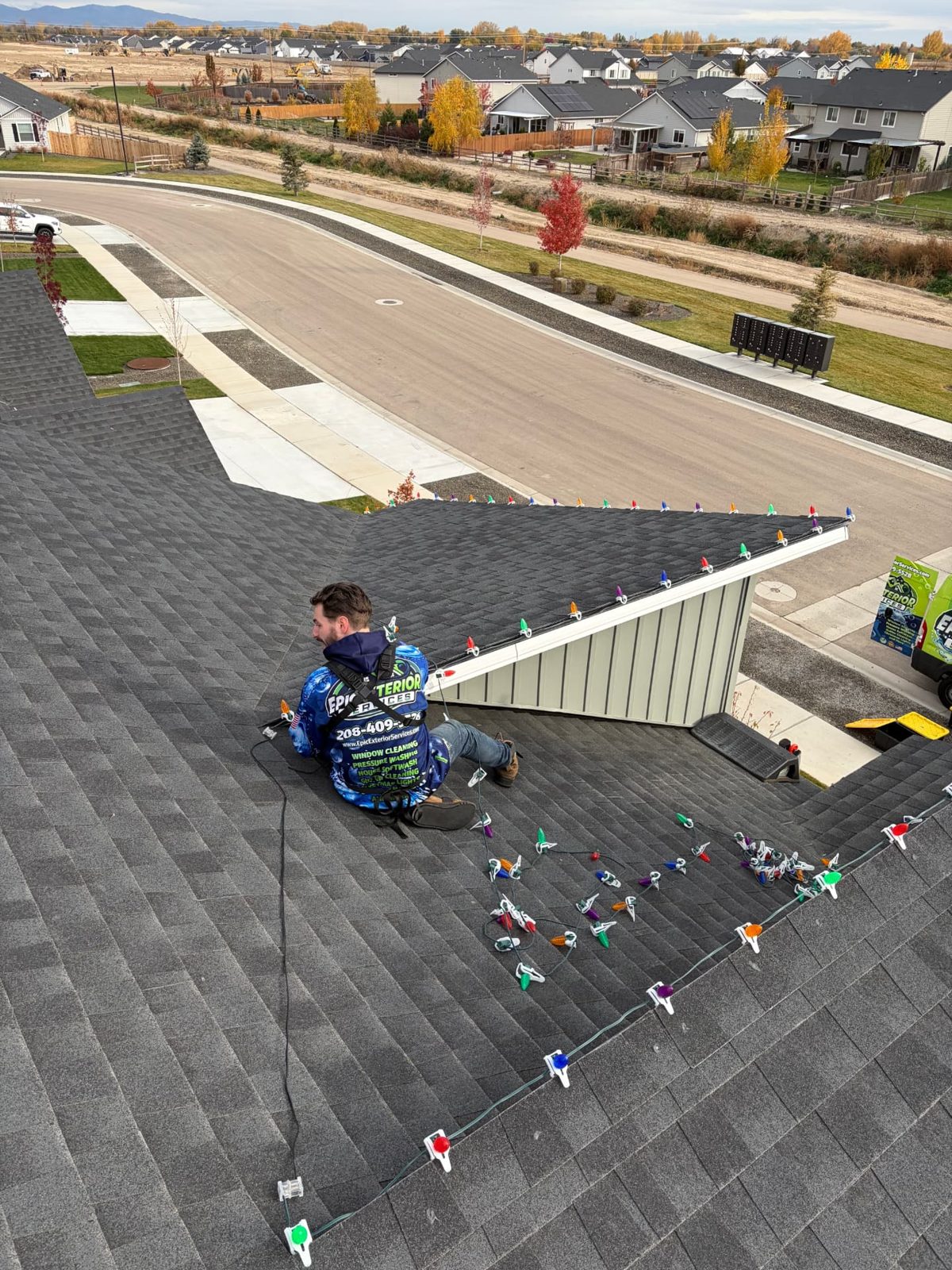 Harnessed Epic Exterior Services installer stringing multicolor C9 bulbs on a Treasure Valley roof