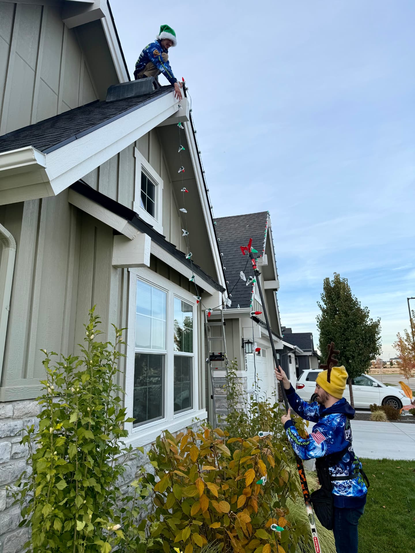 Installer using a light pole to hang red and green C9 bulbs along a gable