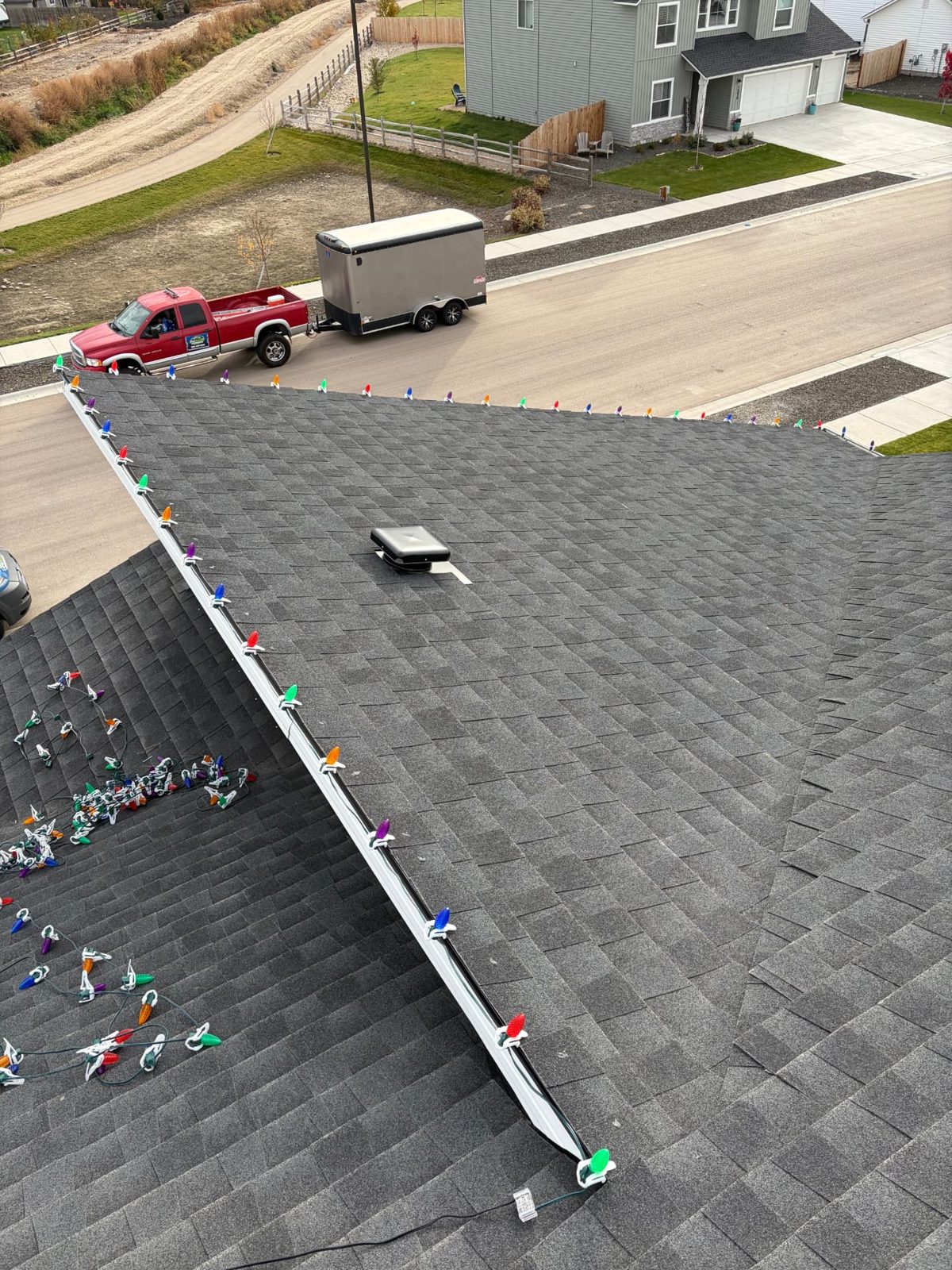 Multicolor C9 Christmas lights clipped evenly along a roof edge and gable, with the crew truck and trailer below